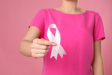 Photo of Woman holding pink ribbon on color background, closeup. Breast cancer awareness