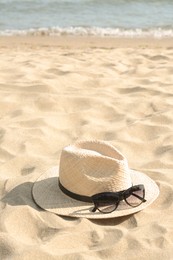 Photo of Hat with beautiful sunglasses on sand near sea. Space for text