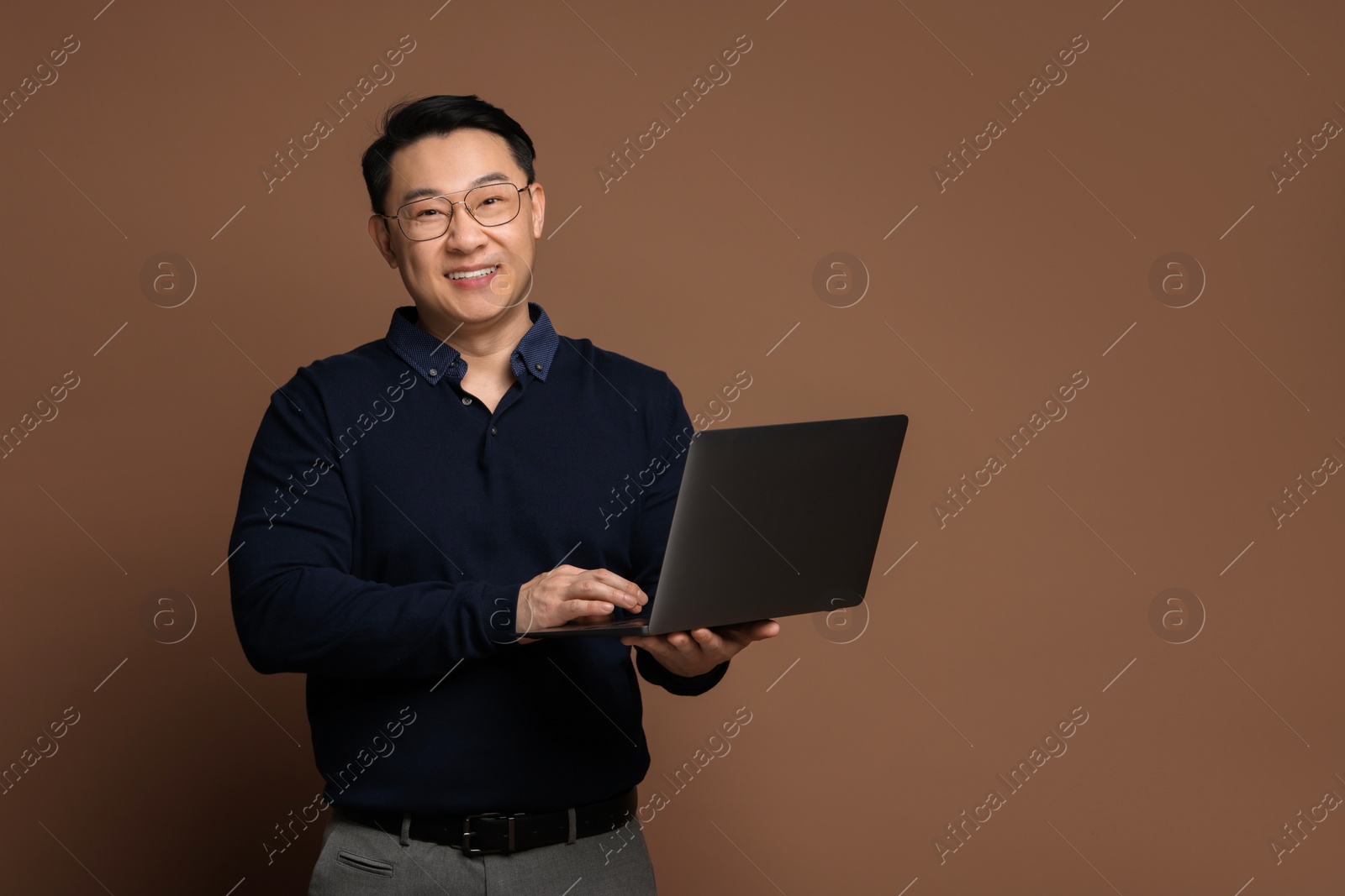 Photo of Portrait of happy man with laptop on brown background. Space for text
