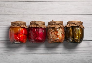 Jars with pickled vegetables on white wooden table, flat lay