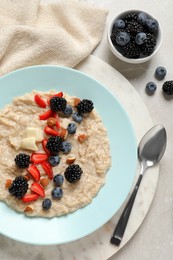 Photo of Tasty oatmeal porridge with berries and almond nuts served on light table, flat lay