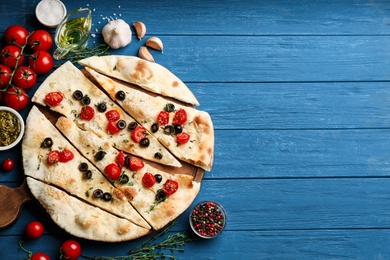 Photo of Delicious focaccia bread with olives and tomatoes on blue wooden table, flat lay. Space for text