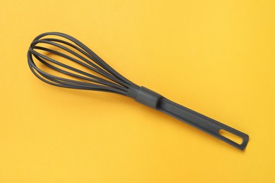 Photo of Plastic whisk on yellow background, top view. Kitchen tool