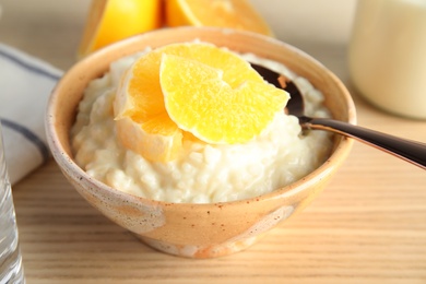 Photo of Creamy rice pudding with orange slices in bowl on wooden table
