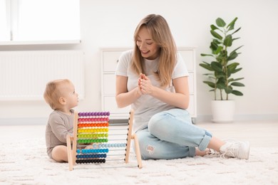 Children toys. Happy mother with her little son and wooden abacus on rug at home