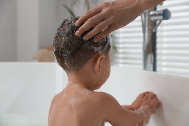 Photo of Mother washing her little son's hair with shampoo in bathroom