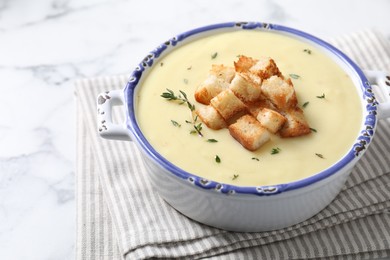 Photo of Tasty potato soup with croutons and rosemary in ceramic pot on white marble table, space for text