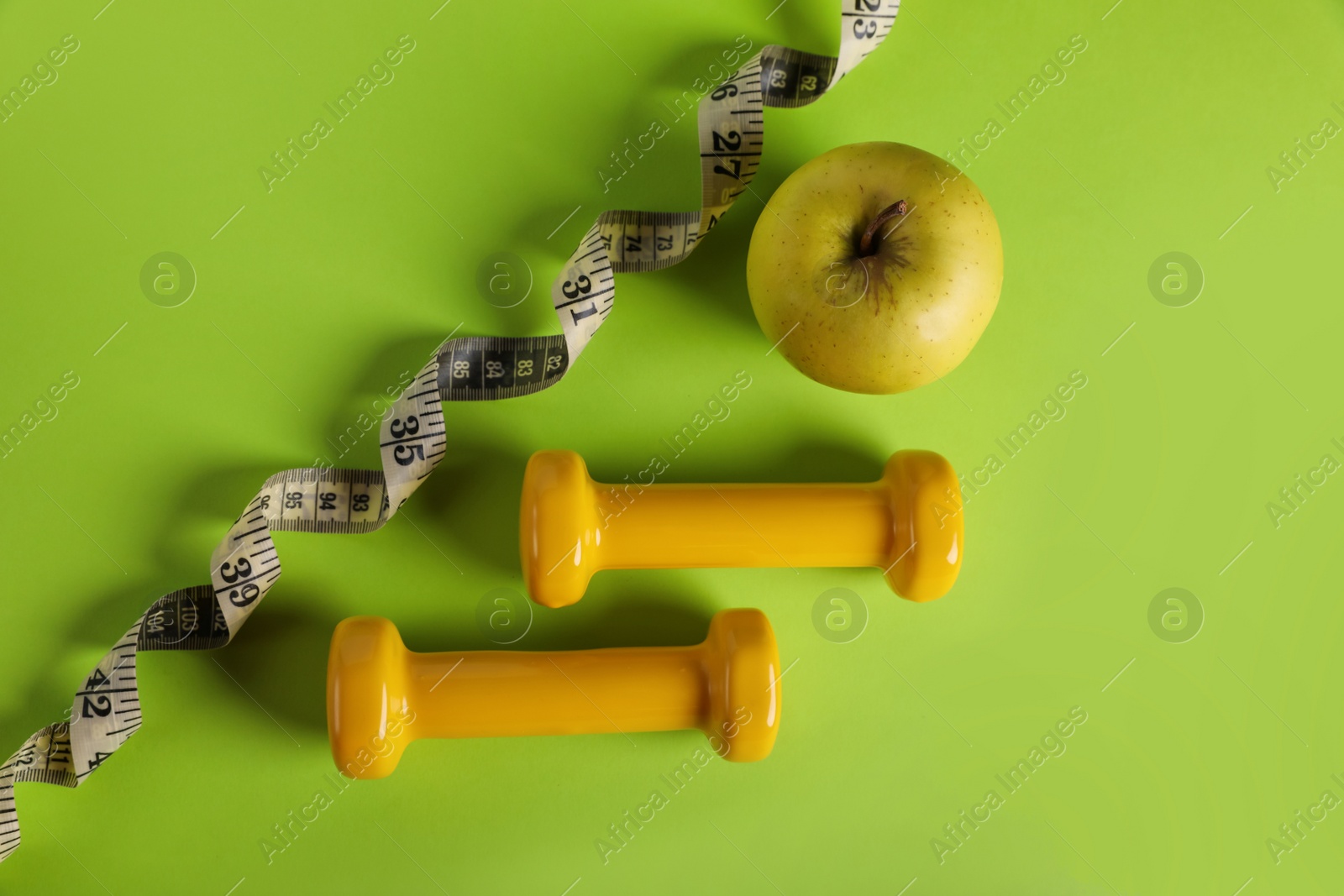 Photo of Measuring tape, dumbbells and apple on light green background, flat lay. Weight control concept