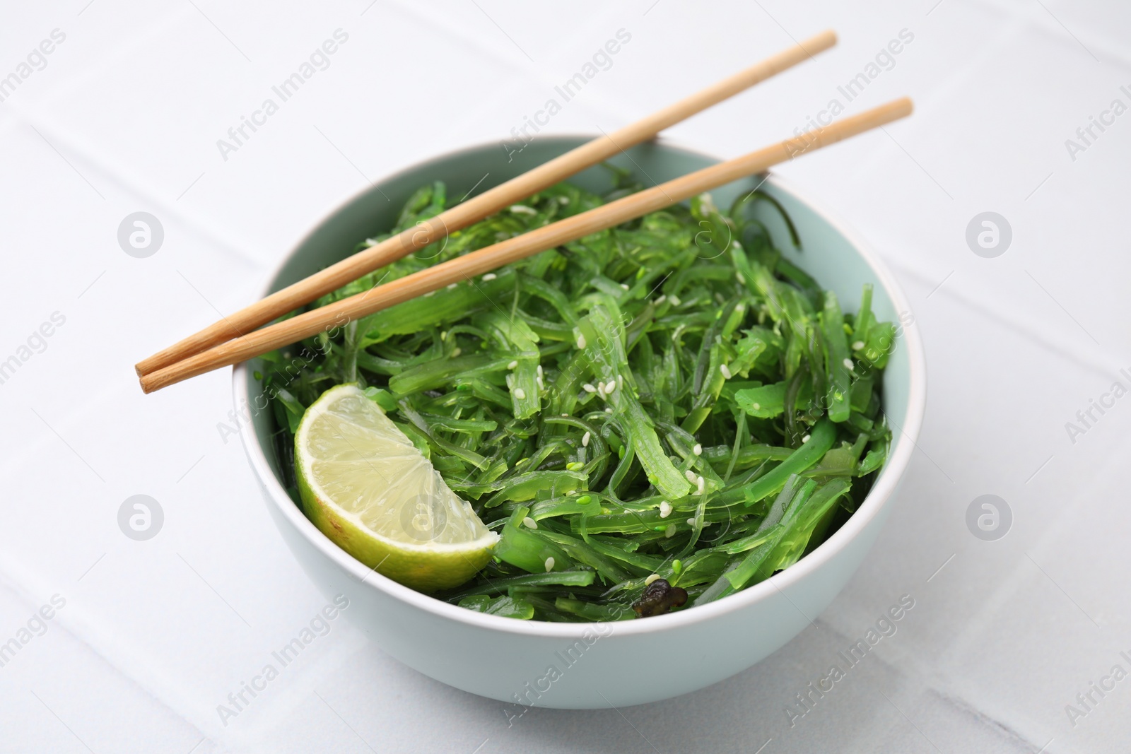 Photo of Tasty seaweed salad in bowl served on white tiled table, closeup