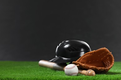 Photo of Baseball bat, batting helmet, leather glove and ball on green grass against dark background. Space for text