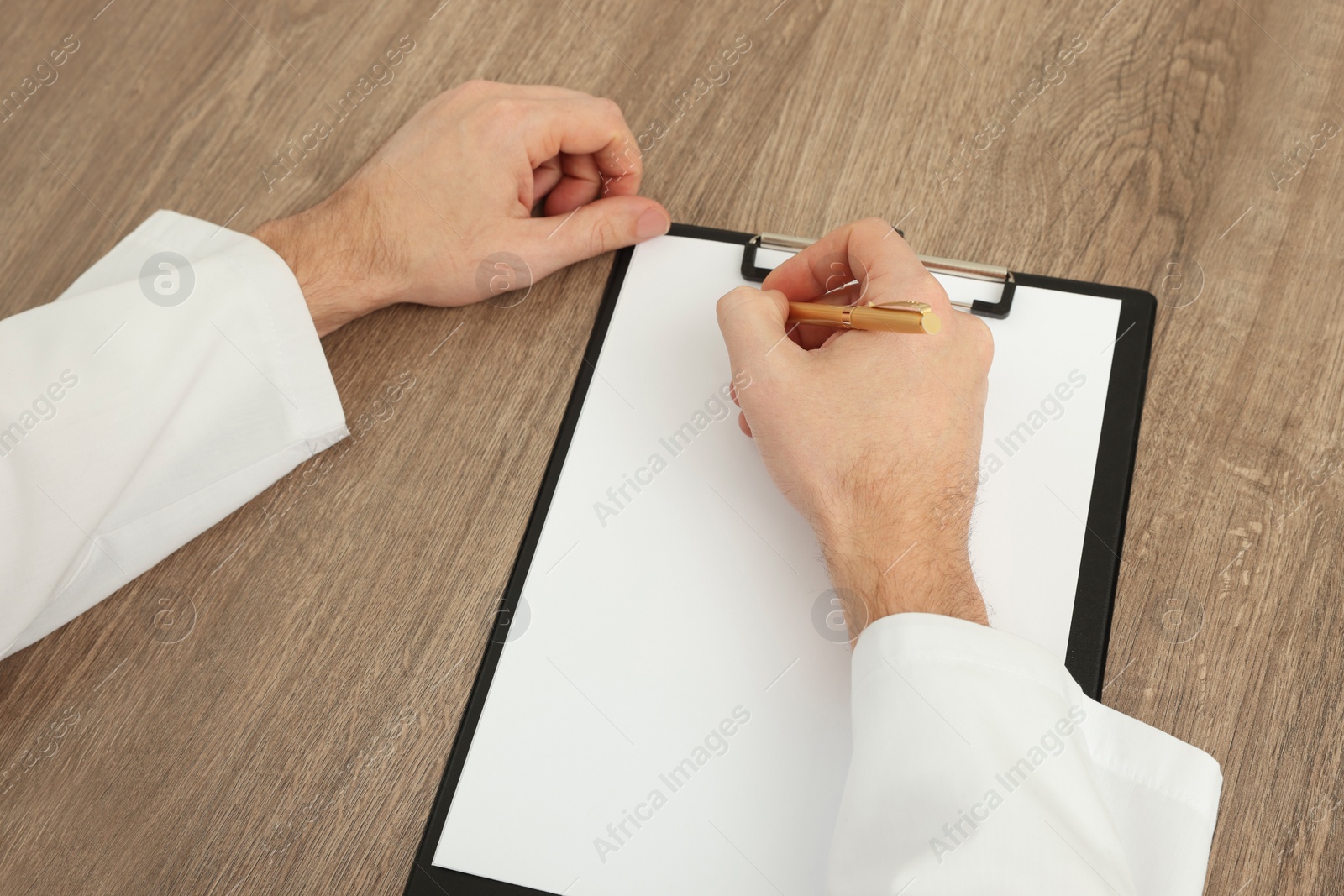 Photo of Doctor writing at wooden table, closeup. Medical service