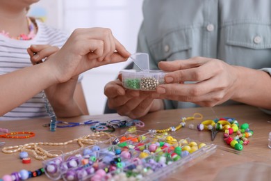 Photo of Mother with her daughter making beaded jewelry at home, closeup