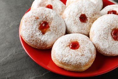 Photo of Delicious donuts with jelly and powdered sugar on black table, closeup