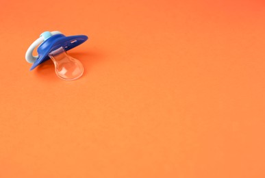 Photo of One blue baby pacifier on orange background. Space for text