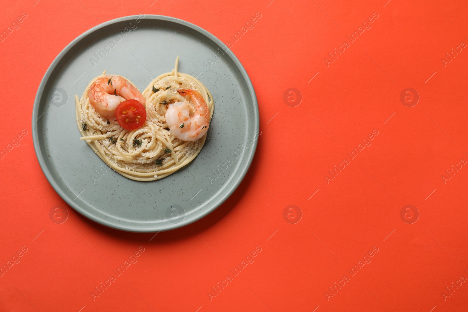 Photo of Heart made of tasty spaghetti, tomato, shrimps and cheese on coral background, top view. Space for text