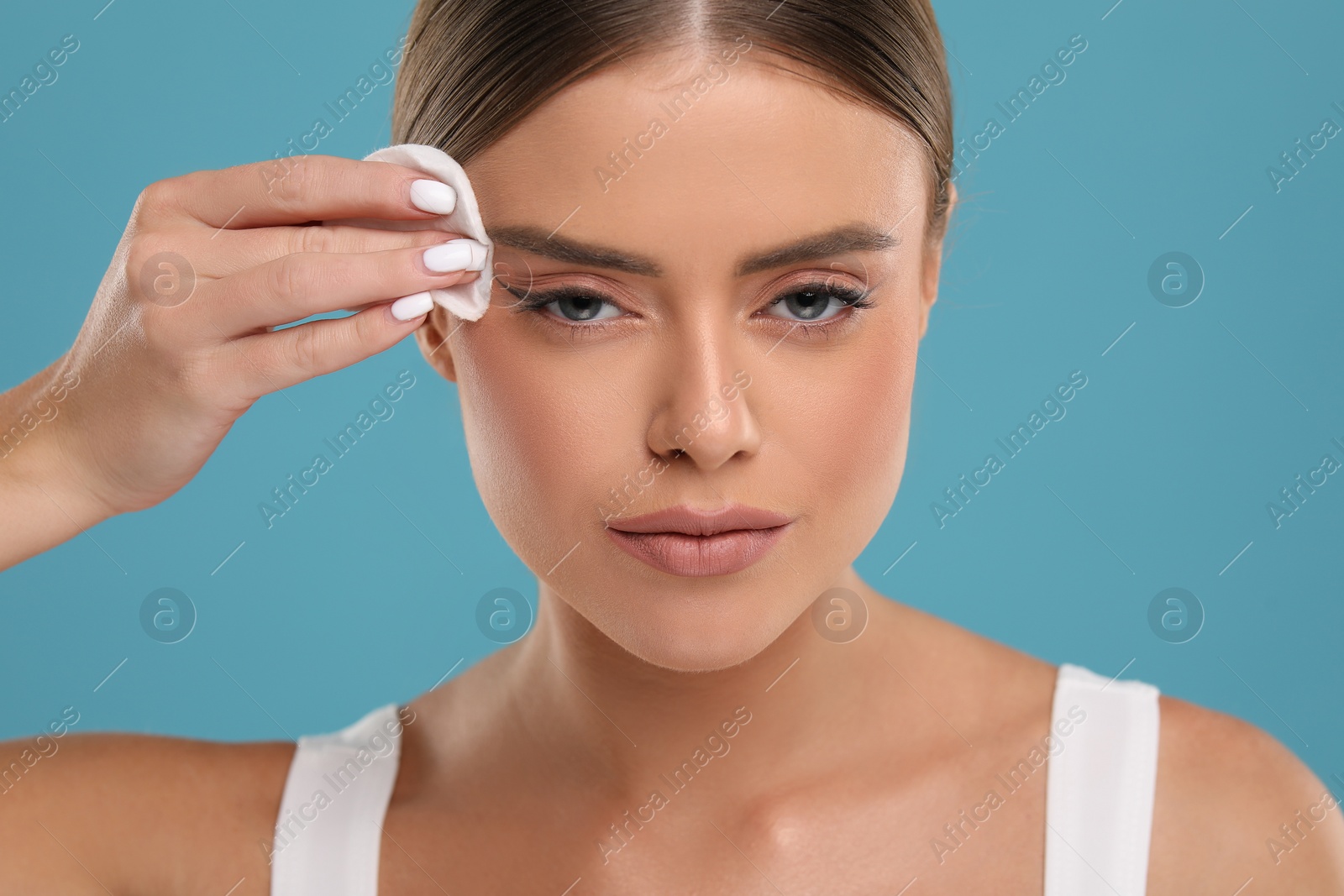 Photo of Beautiful woman removing makeup with cotton pad on light blue background