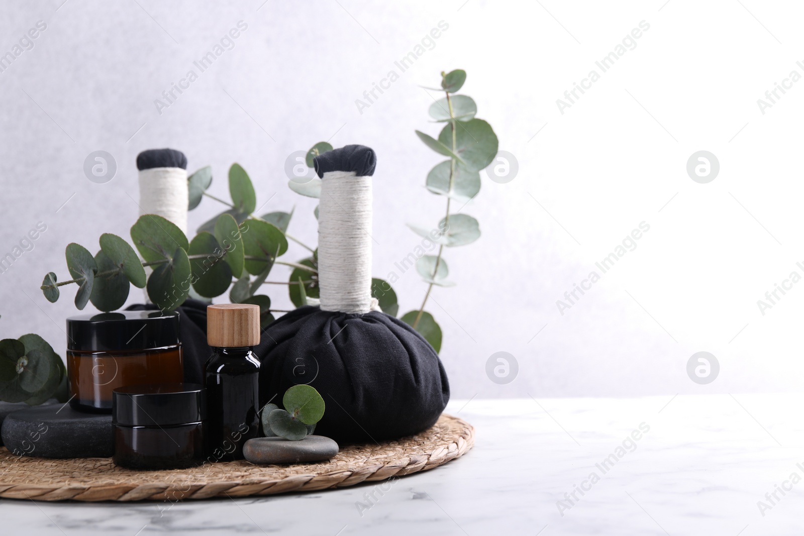 Photo of Spa composition with cosmetic products, herbal massage bags, stones and eucalyptus branches on white marble table, space for text