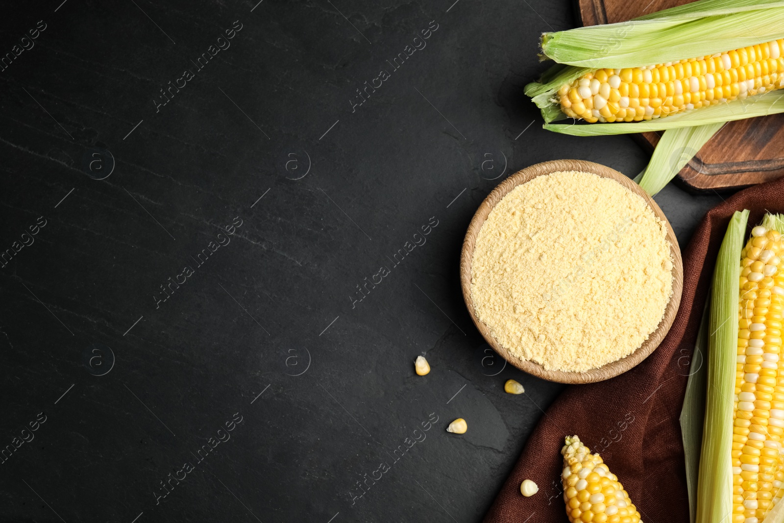 Photo of Corn flour in bowl and fresh cobs on black table, flat lay. Space for text