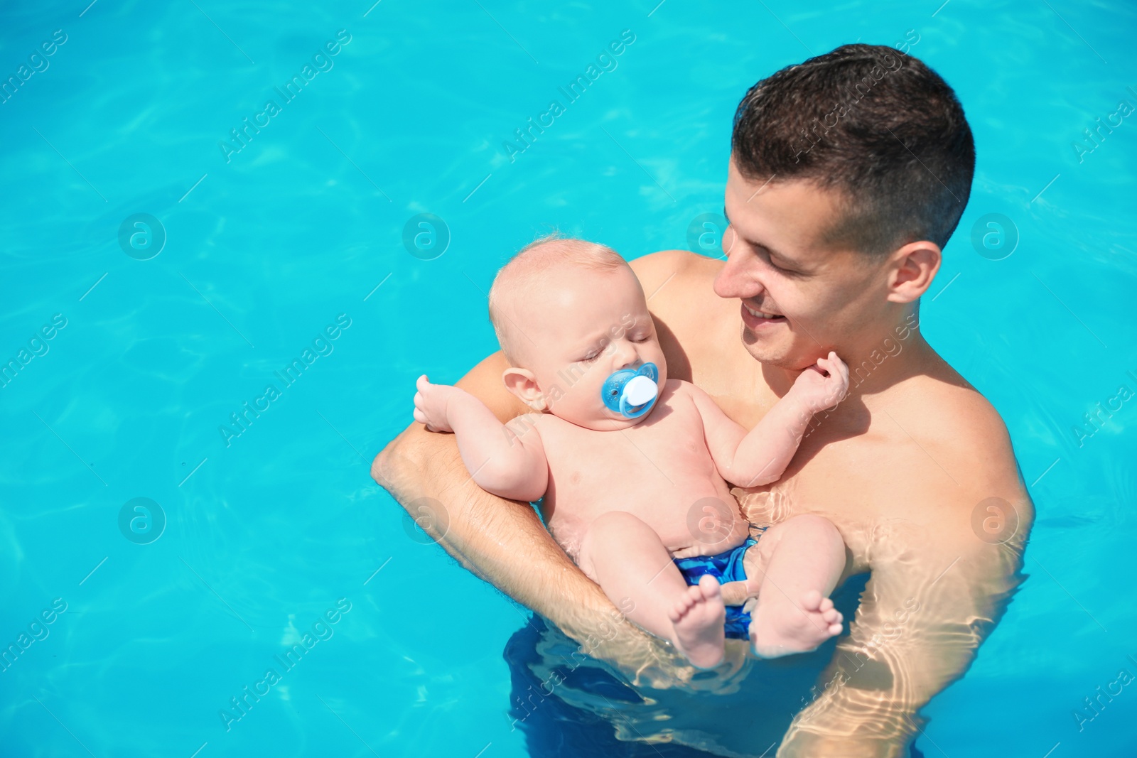 Photo of Man with his little baby in swimming pool on sunny day, outdoors