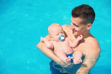 Man with his little baby in swimming pool on sunny day, outdoors