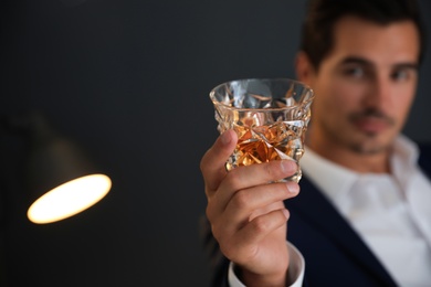 Photo of Young man with glass of whiskey on dark background. Space for text