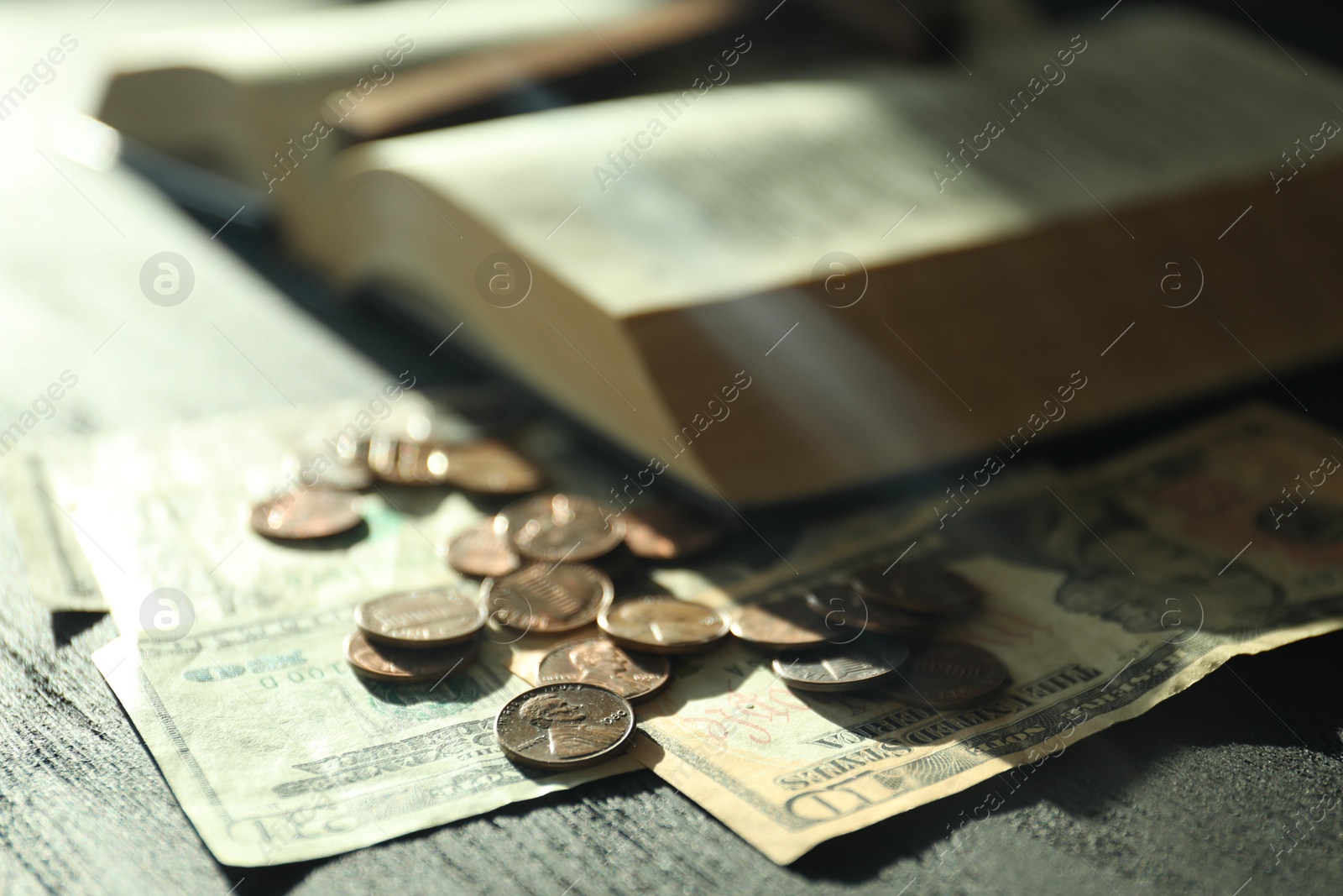 Photo of Donate and give concept. Coins, dollar banknotes and Bible on dark table in sunlights, selective focus