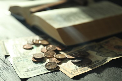 Photo of Donate and give concept. Coins, dollar banknotes and Bible on dark table in sunlights, selective focus