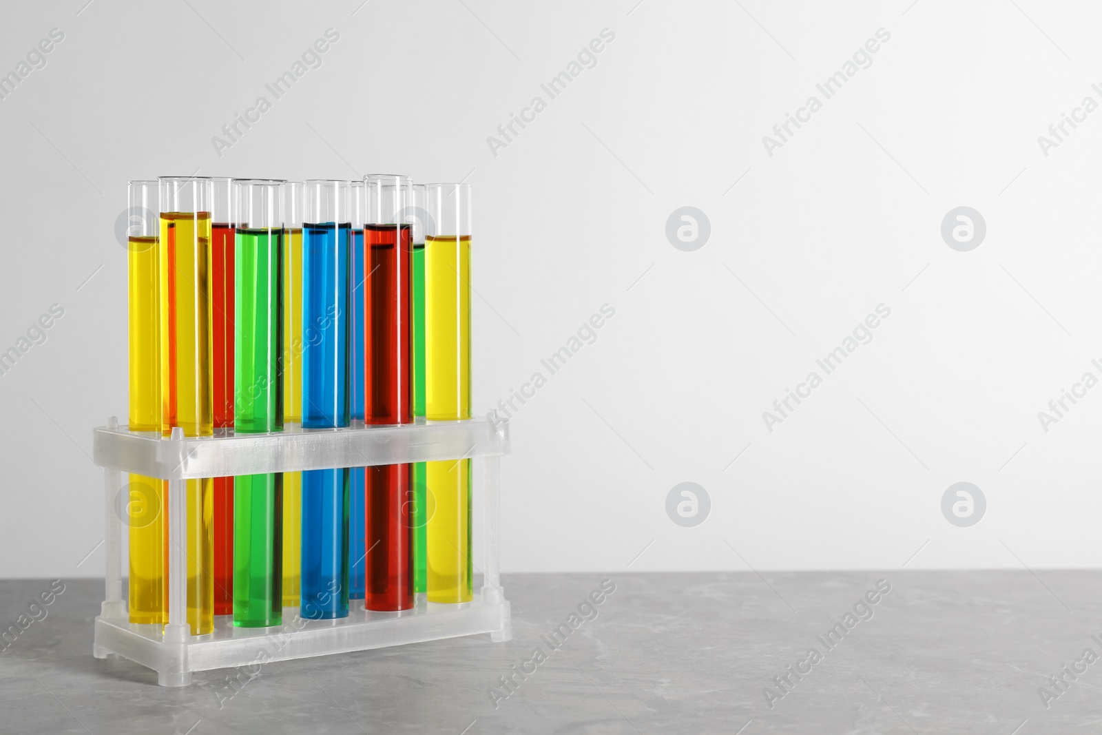 Photo of Test tubes with liquids in stand on grey table against white background, space for text