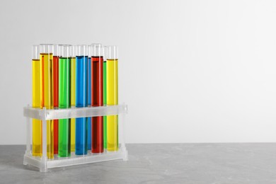 Photo of Test tubes with liquids in stand on grey table against white background, space for text