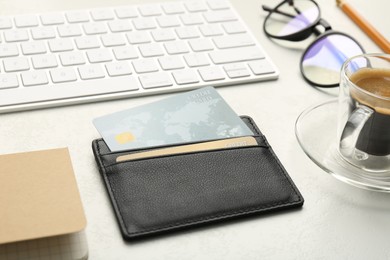 Photo of Leather card holder with credit cards, glasses, keyboard and coffee on white table, closeup