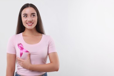 Photo of Beautiful young woman with pink ribbon on white background, space for text. Breast cancer awareness