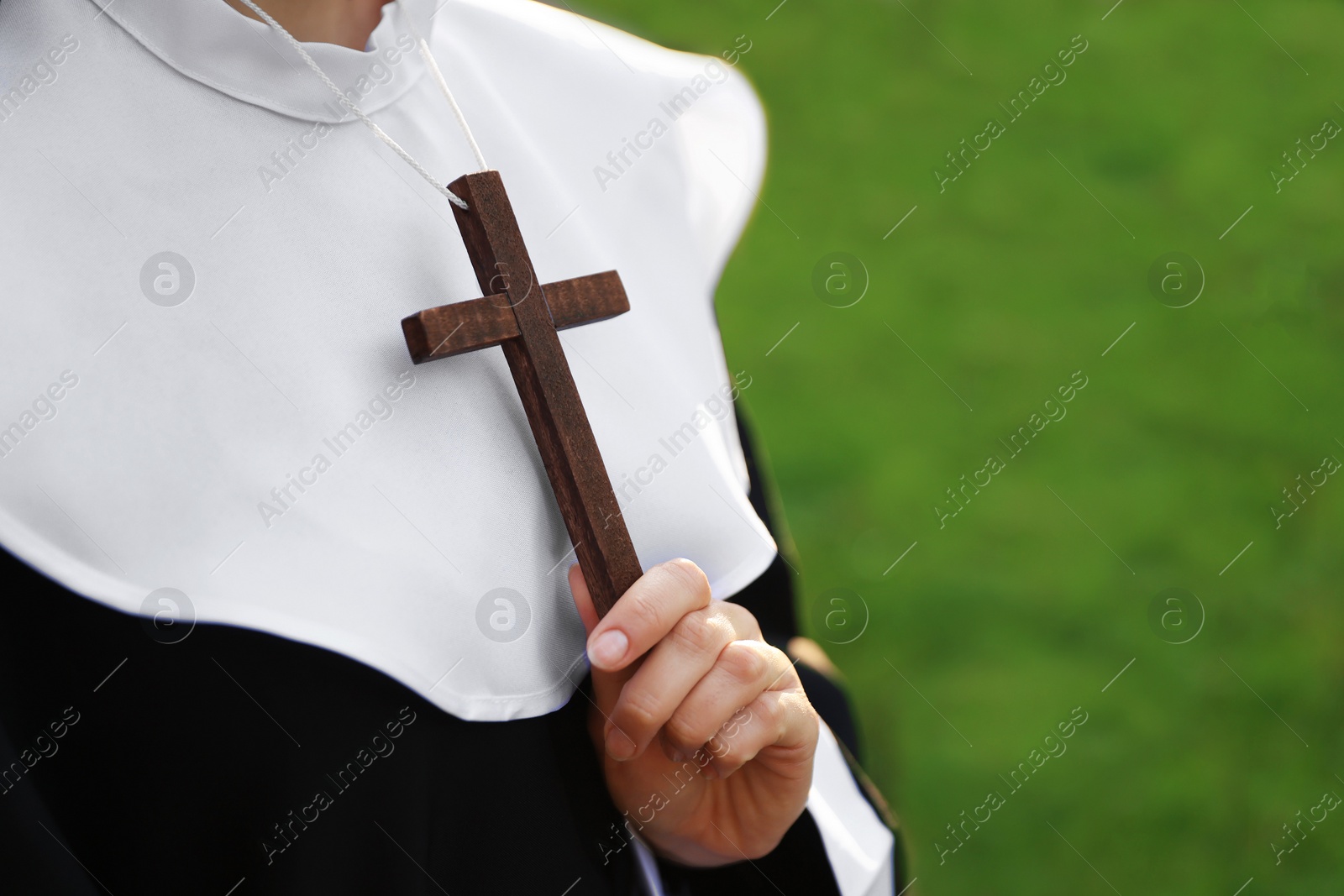 Photo of Young nun with Christian cross outdoors on sunny day, closeup. Space for text