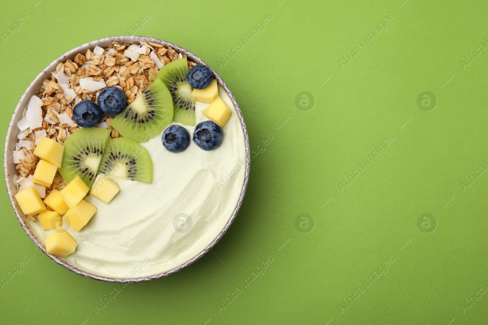 Photo of Tasty matcha smoothie bowl served with fresh fruits and oatmeal on green background, top view with space for text. Healthy breakfast