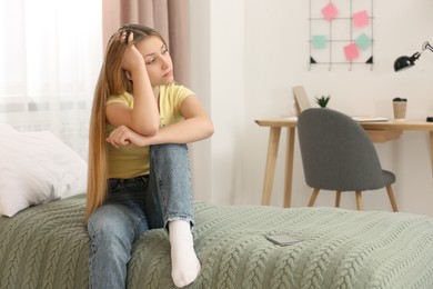 Photo of Upset teenage girl sitting alone on bed at home