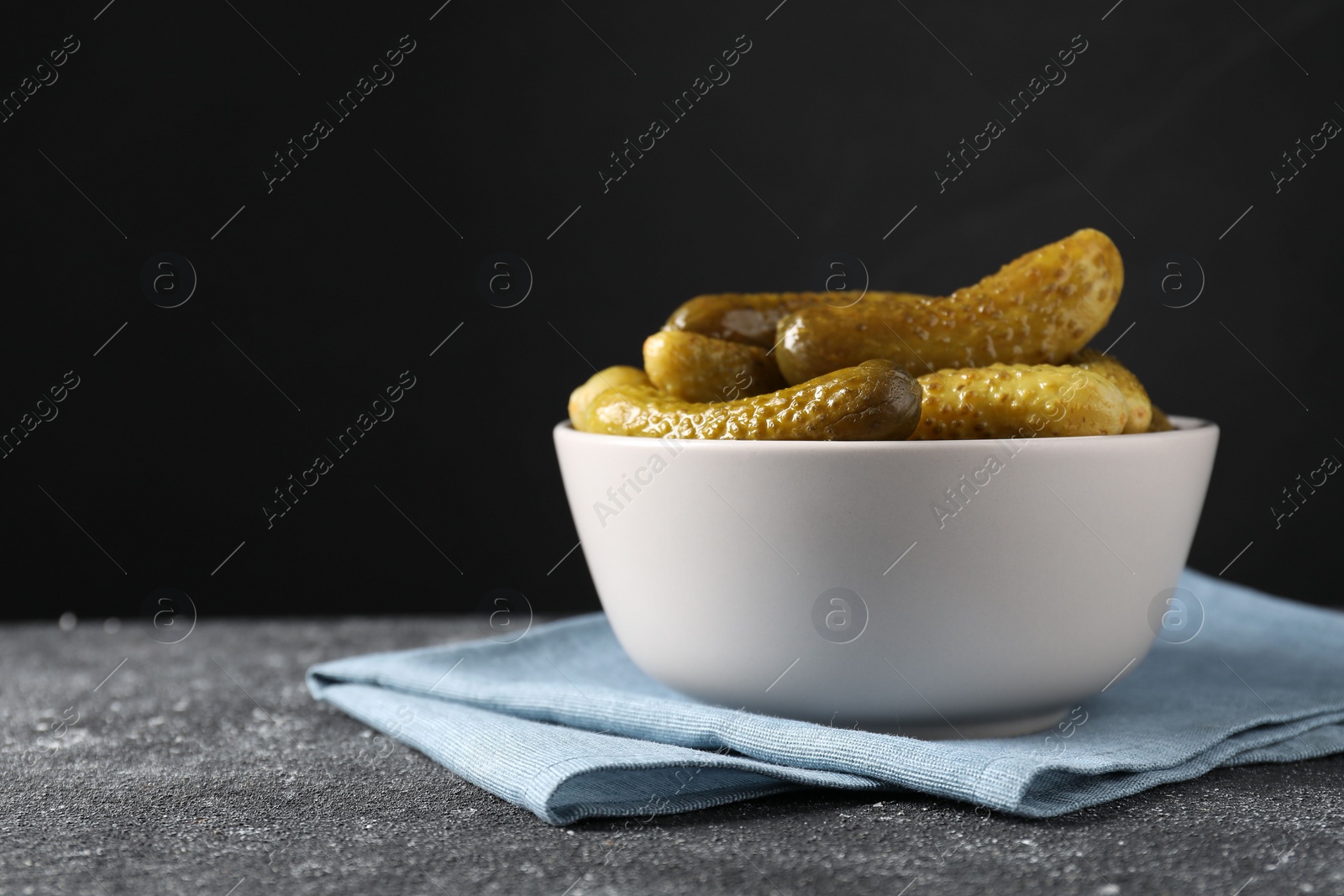 Photo of Tasty pickled cucumbers in bowl on grey textured table, space for text