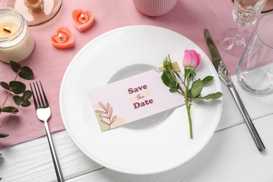 Romantic place setting with floral decor and candles on white wooden table, above view