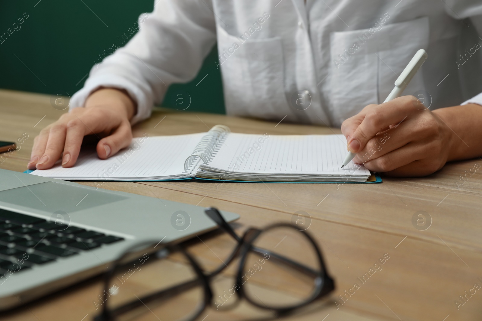 Photo of Left-handed woman writing in notebook at wooden table, closeup