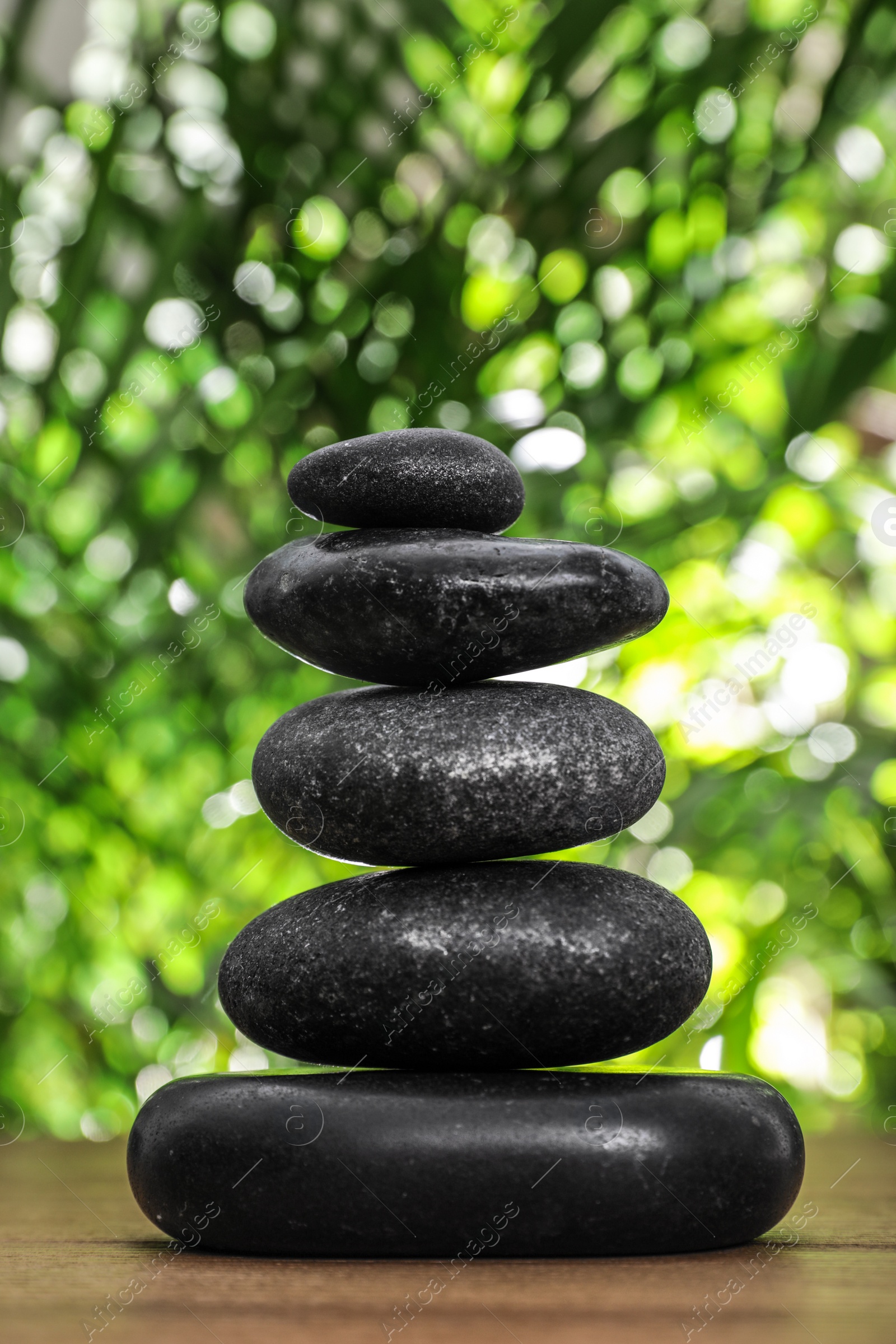 Photo of Table with stack of stones and blurred green leaves on background. Zen concept