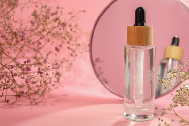 Bottle of face serum and beautiful flowers near mirror on pink background, closeup. Space for text