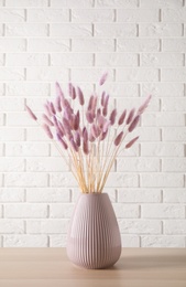 Photo of Dried flowers in vase on table against white brick wall