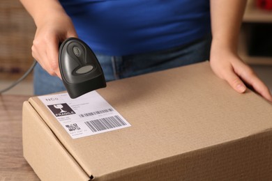 Photo of Post office worker with scanner reading parcel barcode at counter, closeup