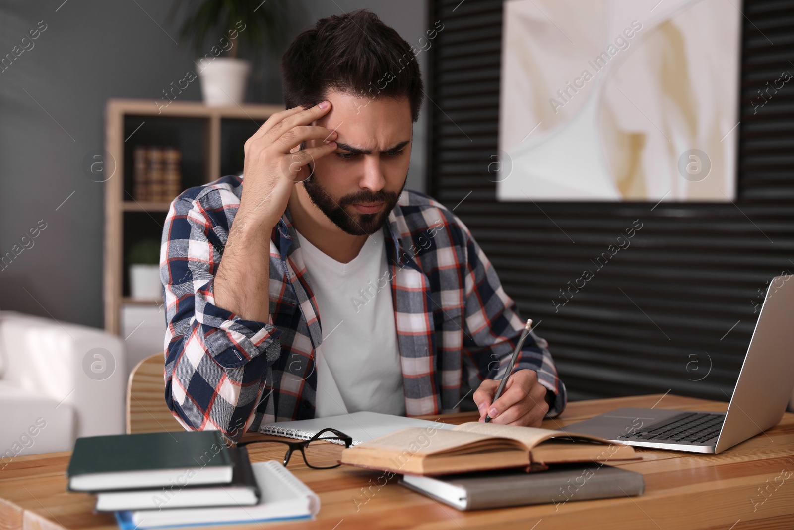 Photo of Confused young man writing down notes during webinar at table in room