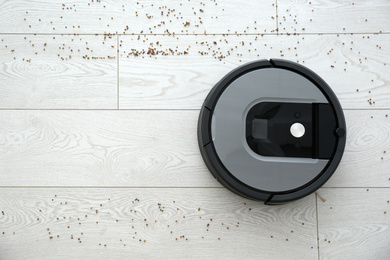 Photo of Modern robotic vacuum cleaner removing scattered buckwheat from wooden floor, top view. Space for text