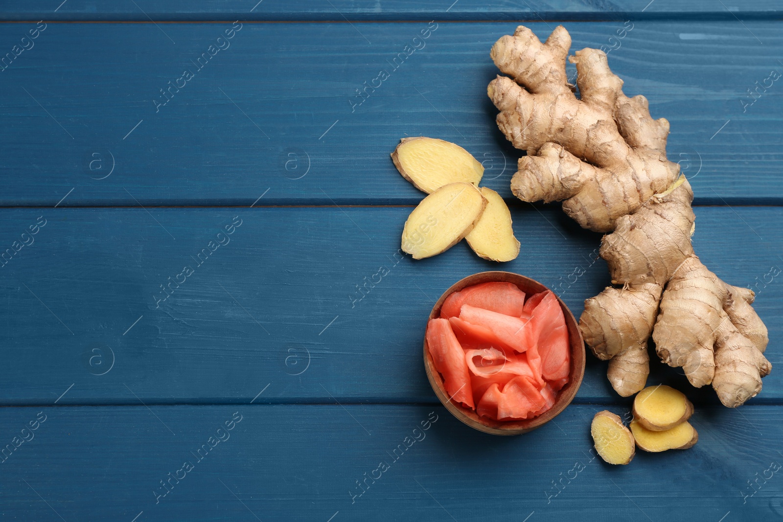 Photo of Spicy pickled ginger and root on blue wooden table, flat lay. Space for text