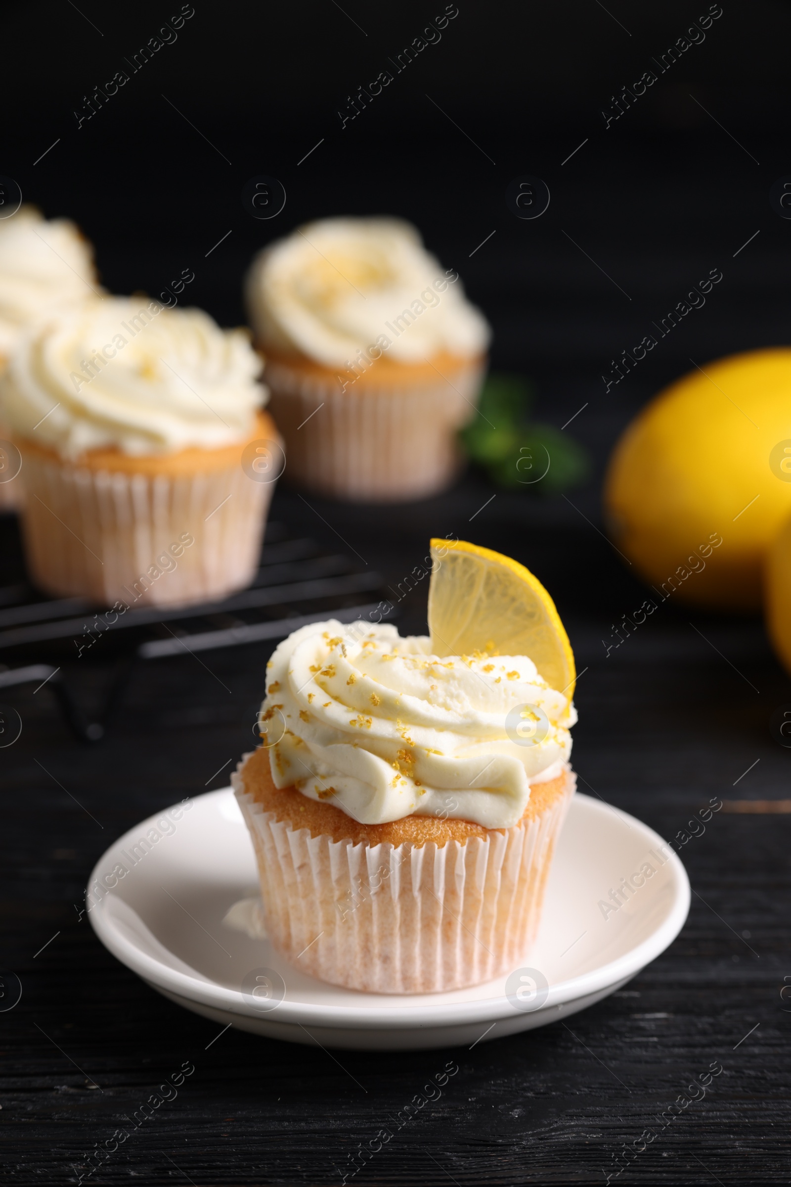 Photo of Delicious cupcake with white cream and lemon zest on black wooden table, closeup