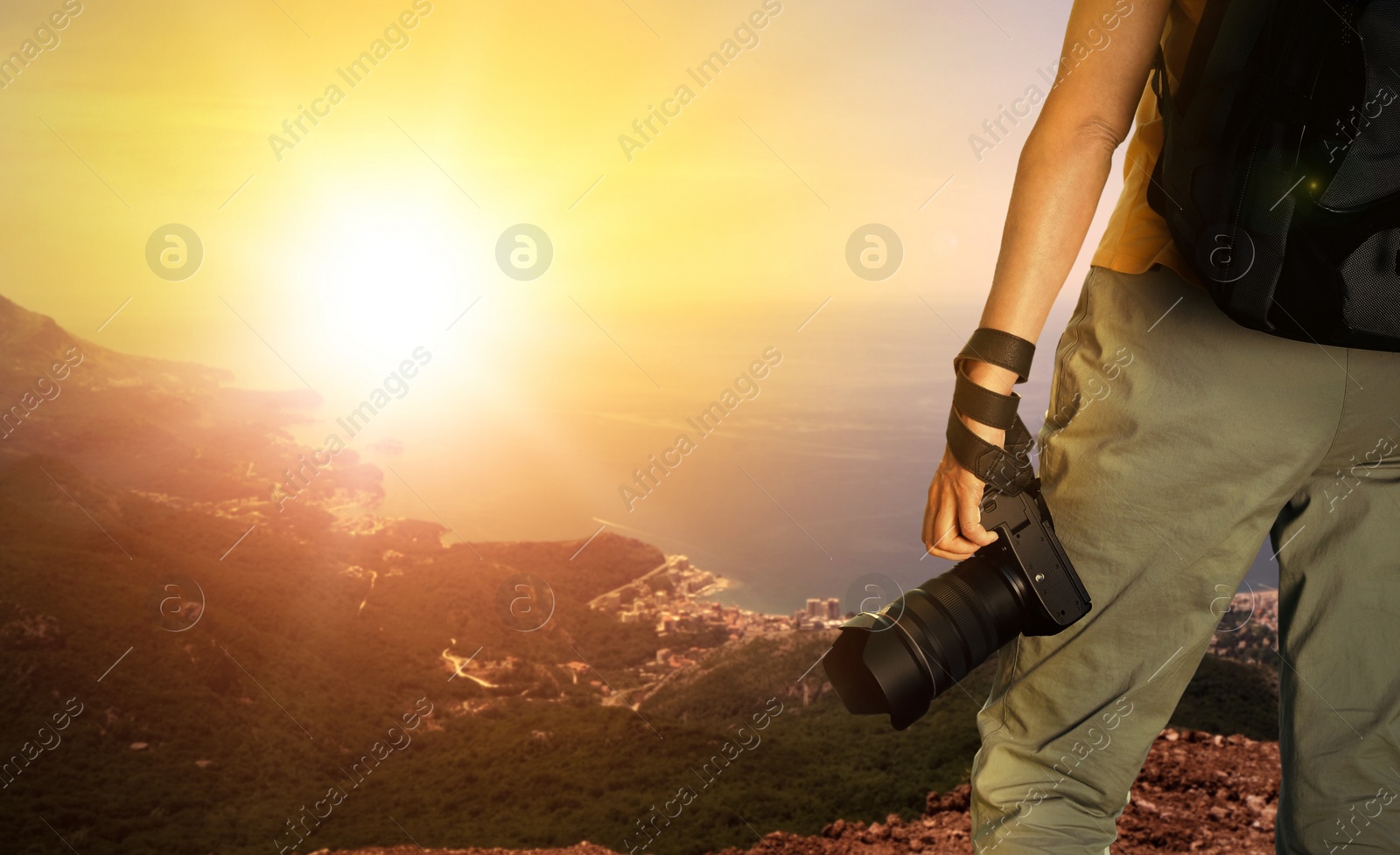 Image of Photographer holding professional camera and beautiful view of mountains and sea at sunset on background, space for text