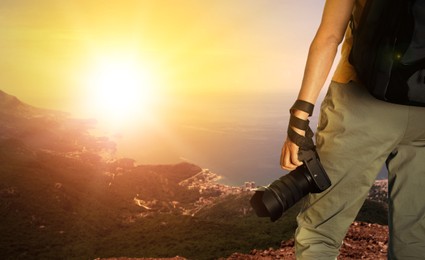 Photographer holding professional camera and beautiful view of mountains and sea at sunset on background, space for text