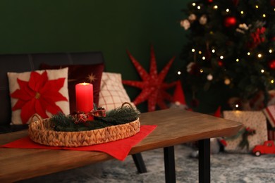 Wicker tray with red candle and fir branches on wooden table indoors, space for text. Christmas decor