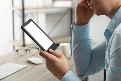 Photo of Man using e-book reader at table indoors, closeup