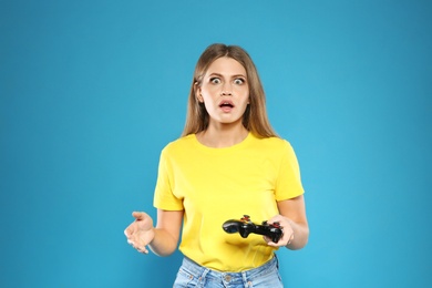 Emotional young woman playing video games with controller on color background